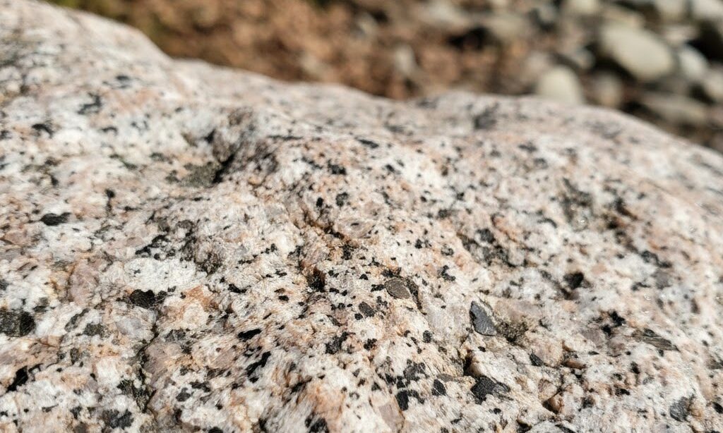 白やピンクの粒と黒い斑点が混ざる花崗岩の表面を拡大した実写風画像。火成岩の特徴がわかる自然石の質感。