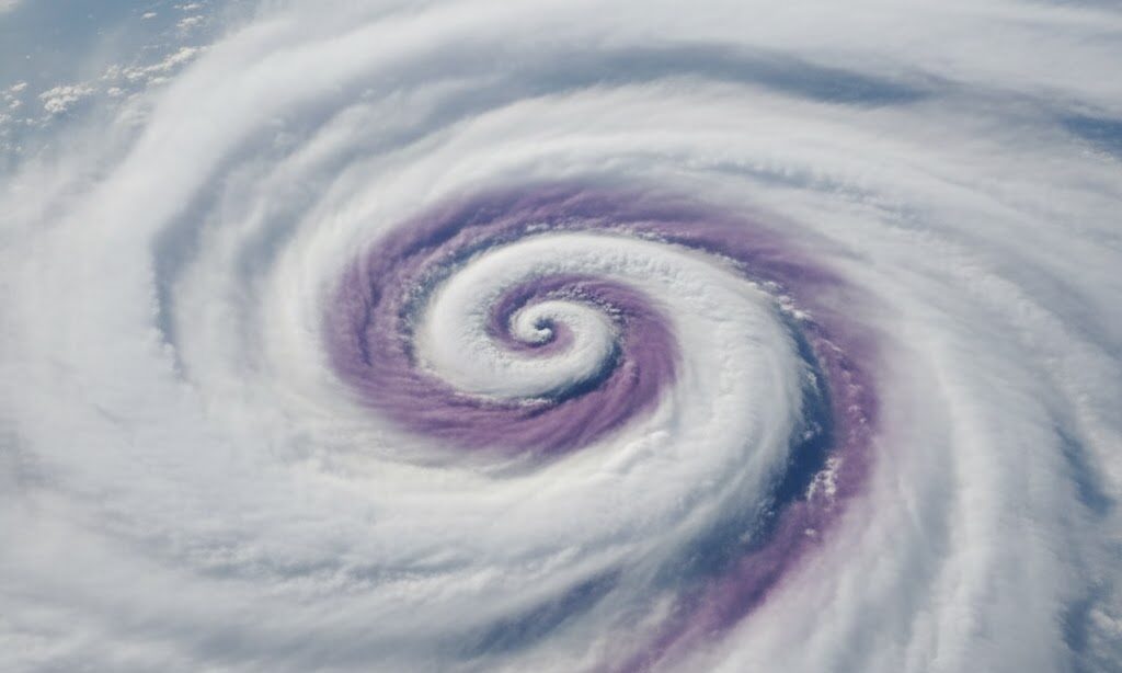 紫がかった雲が重なり渦を巻く日本の空を実写風で表現。閉塞前線と低気圧の終息を穏やかに示す教育的イメージ。