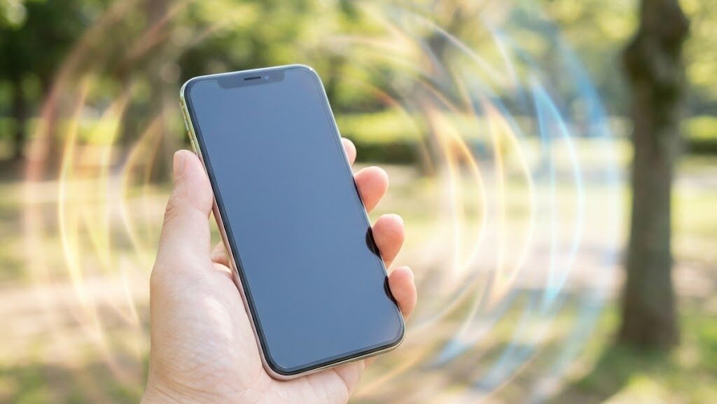 日本人の手に持たれたスマートフォンと、電波の揺らぎを示す抽象表現の実写風画像