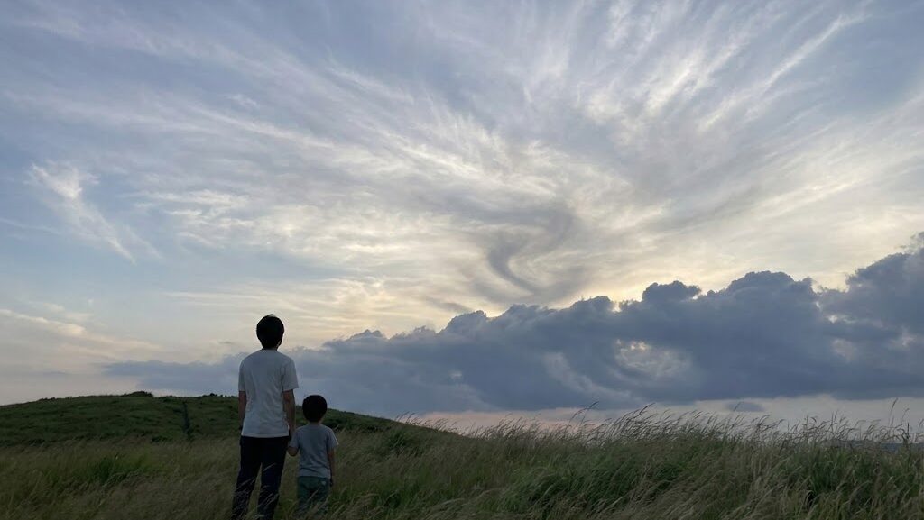 台風接近前の空を見上げる日本人親子の後ろ姿。巻雲が広がる静かな空の変化から、天気悪化の予兆を学べる実写風イメージ。