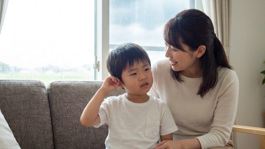 台風時の気圧変化による耳の違和感に対し、家族が室内で落ち着いて対応している様子