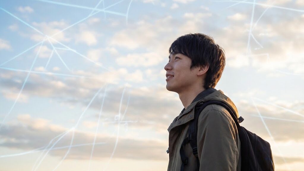 空を見上げて考える学生と、背後に浮かぶ抽象的な光のライン。宇宙の成り立ちを科学的に考える様子。