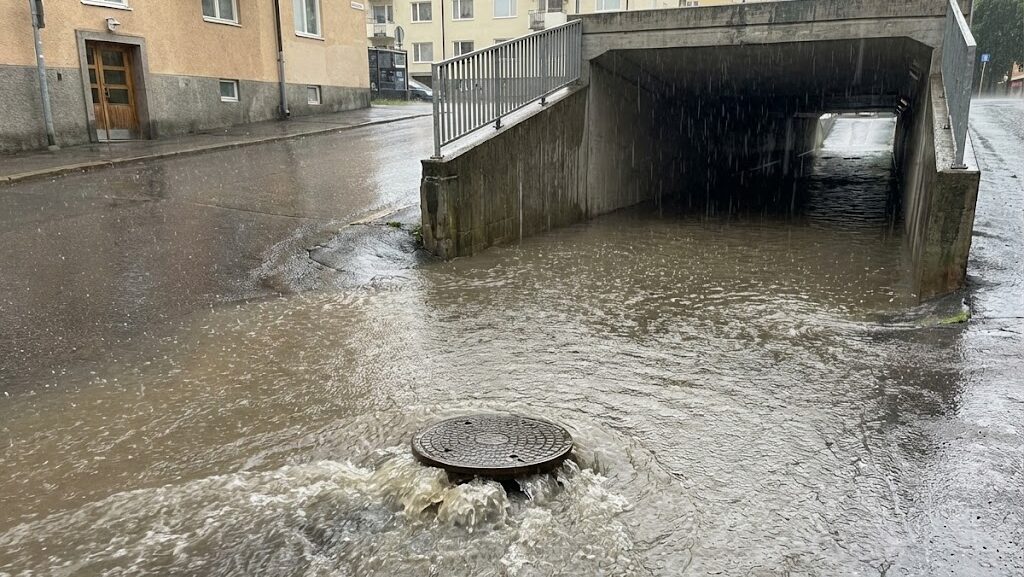 激しい雨で排水口やマンホールから水があふれ出しそうになっている都市冠水の実写風イメージ