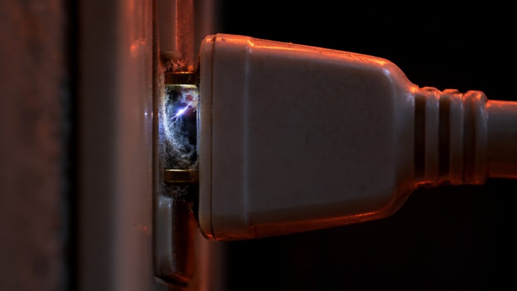 ほこりのたまった電源プラグの間に小さな火花が走るトラッキング現象のイメージ